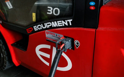 Close-up of a red electric forklift with charging port, featuring brand logos and connection cable.