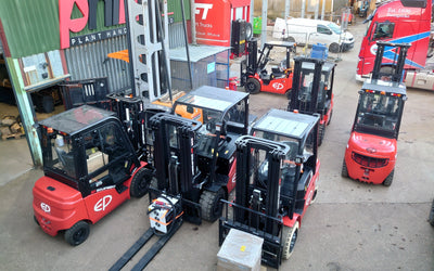 Several red and black forklifts are arranged in a yard outside a warehouse with