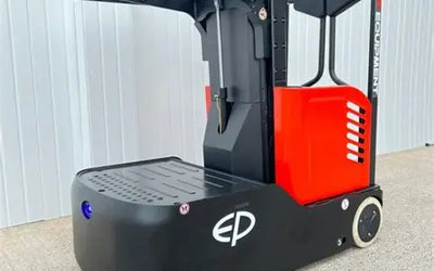 A compact electric pallet jack in black and red, featuring a raised platform and ergonomic design, set against a metal backdrop.