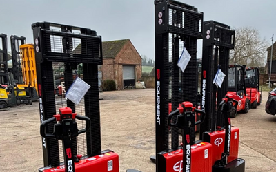 Three red EP Equipment stackers are lined up on a concrete surface, with a cloudy sky and storage buildings in the background.