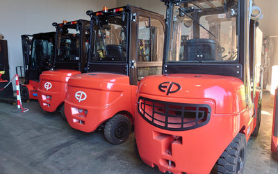 Three bright red forklifts are lined up in a garage, each with clear cabins and distinctive branding on the front. The setting is well-lit and orderly.