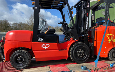 Red EP Equipment 35 Li-Ion forklift loaded on a trailer with straps securing it, under a partly cloudy sky.
