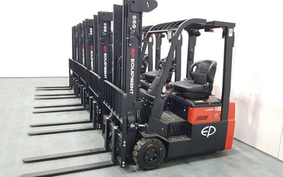 A row of electric forklifts lined up against a white wall, showcasing their black and red design, with visible forks extended.