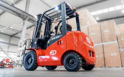 Red forklift parked indoors near stacked wooden crates in a spacious, well-lit warehouse environment.