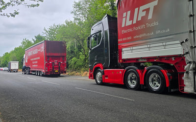 Two large trucks parked on a tree-lined road, one red with 