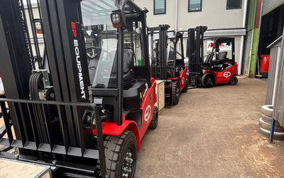Four red EP Equipment forklifts parked in a row outside an industrial building under a cloudy sky.