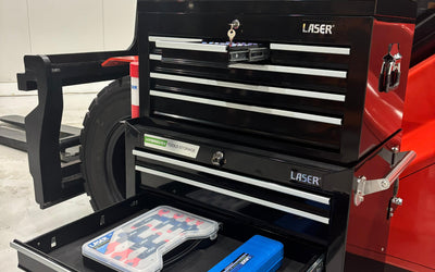 Black multi-drawer LASER tool chest with keys in lock, open drawers displaying toolkits, positioned in front of a forklift in a workshop.