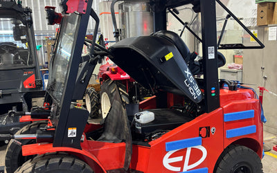 Red electric forklift with open hood inside a warehouse, showing engine compartment, with Union Jack and Turkish flags hanging above.