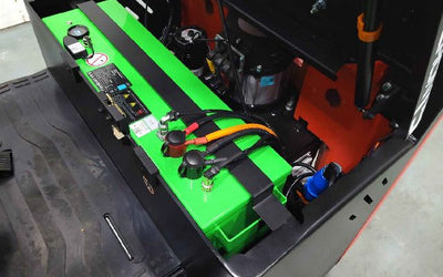 Green battery installed inside a black industrial machine with connected power cables and secured by metal straps.