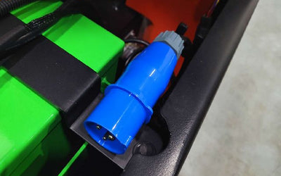 Blue industrial power plug attached to a green and black device inside a metal frame.