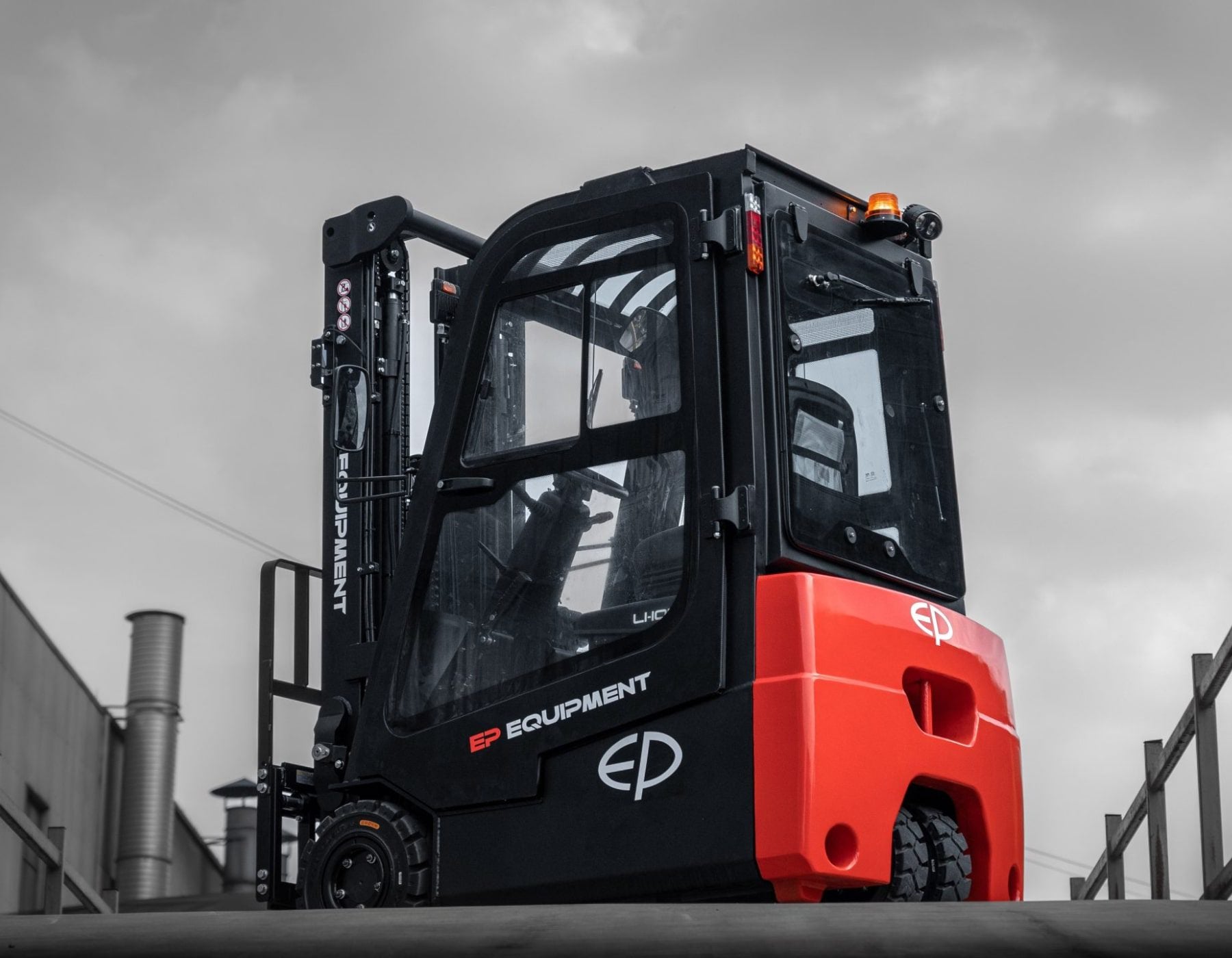 Red and black EP electric forklift with an enclosed cab, shown on an outdoor ramp with overcast skies in the background, highlighting its robust and weather-resistant design.