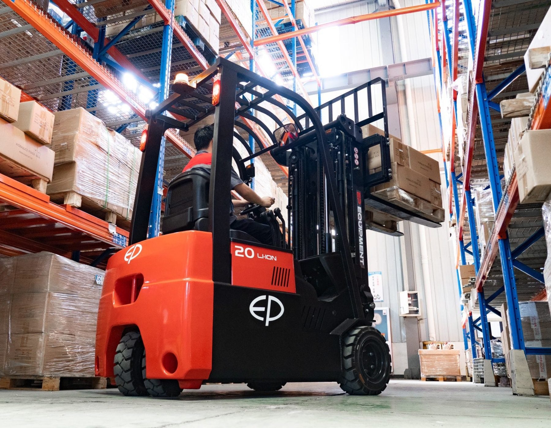 Operator driving a red and black EP electric forklift, lifting a loaded pallet towards high warehouse shelves, surrounded by neatly stacked boxes and industrial shelving.