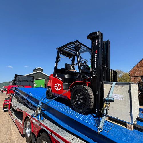 Red and black forklift on a flatbed truck with a clear blue sky.