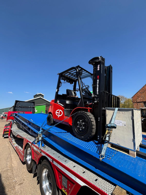Red and black forklift on a flatbed truck with a clear blue sky.