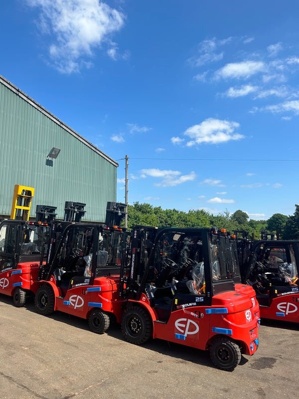 Multiple Formula 1 cars on a trailer with a blue sky and building in the background