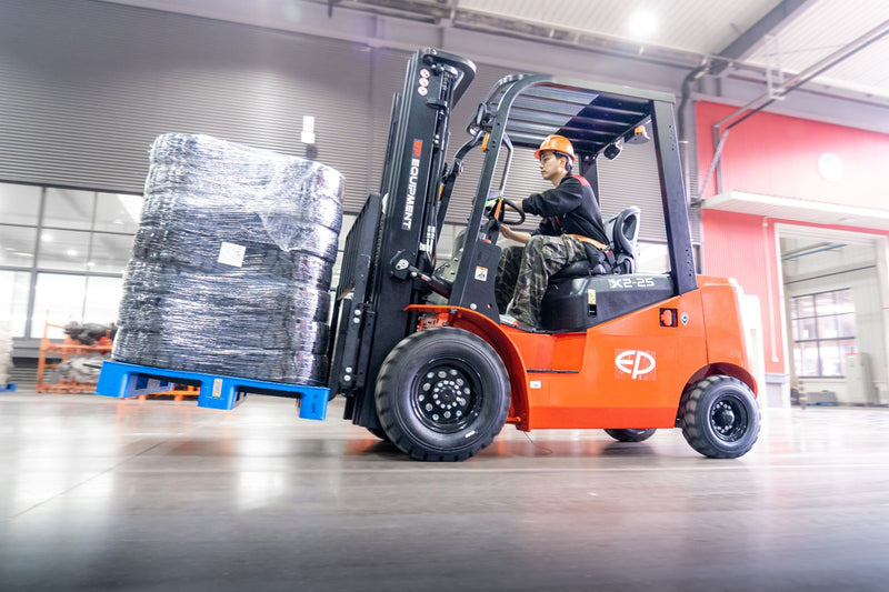 Person operating an orange forklift with a pallet of goods inside a warehouse.