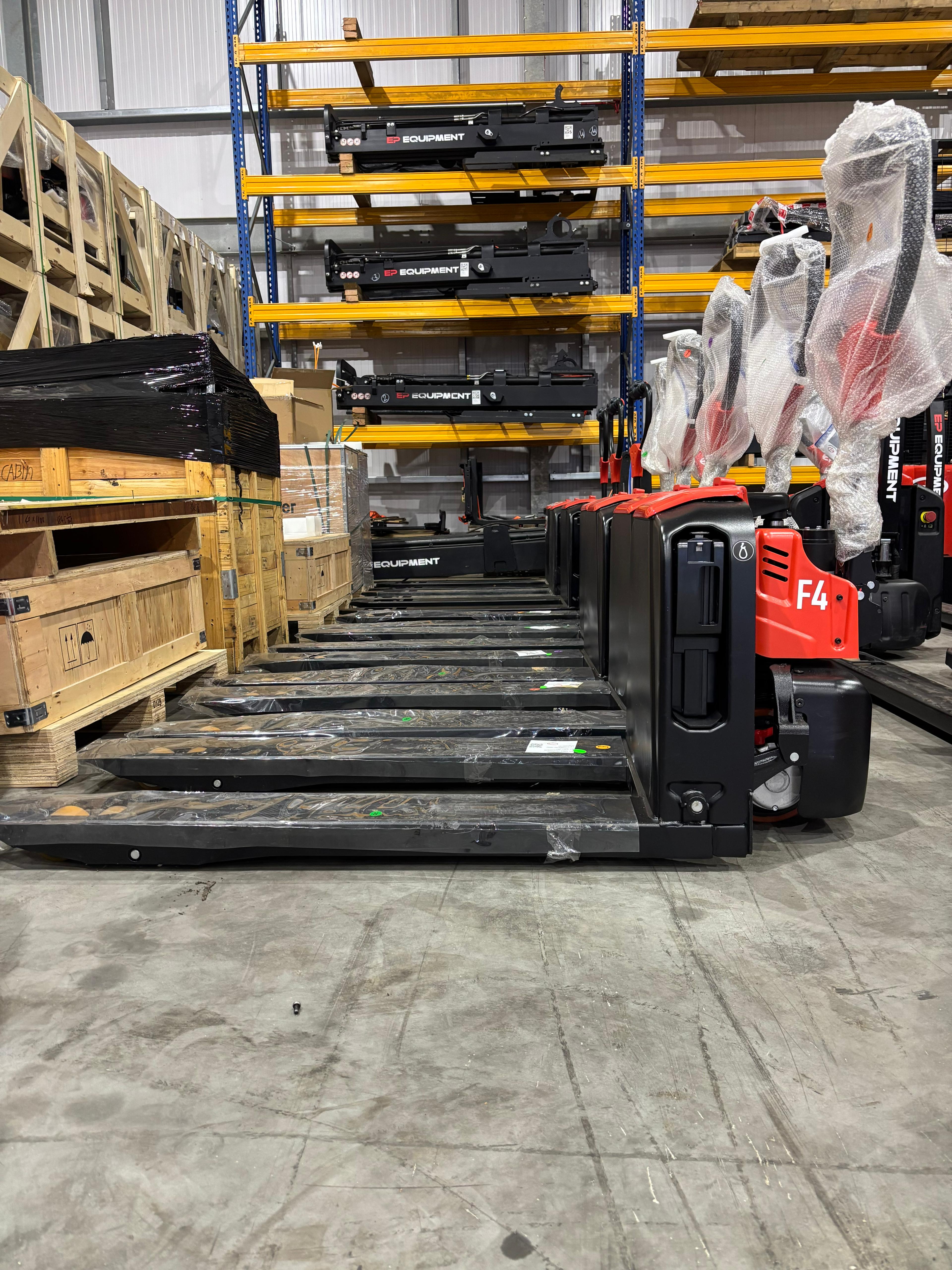 Warehouse interior showing organized rows of pallet jacks in red and black, with shelving holding equipment in the background. A clean, industrial setting.