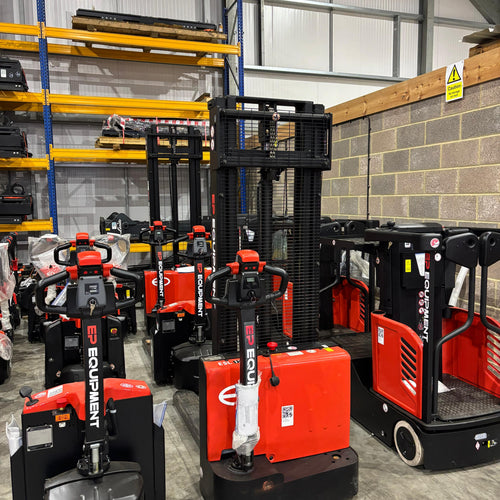 Red and black forklifts in a warehouse setting with shelves and concrete walls.