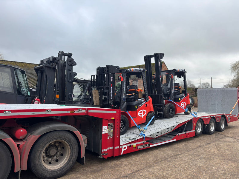 Red flatbed truck with forklifts on a cloudy day