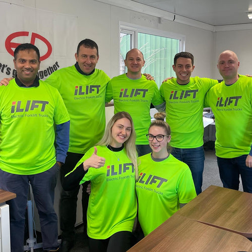 A group of six individuals wearing bright green iLIFT t-shirts pose together in a modern office setting.