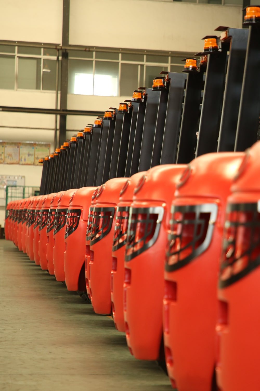 Row of red forklifts lined up neatly in a warehouse, each with an amber warning light on top, creating a uniform and organized display.