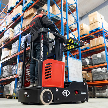 Warehouse worker operating a red electric order picker by EP Equipment, standing at the controls and maneuvering near blue shelving filled with boxed inventory in a busy warehouse.